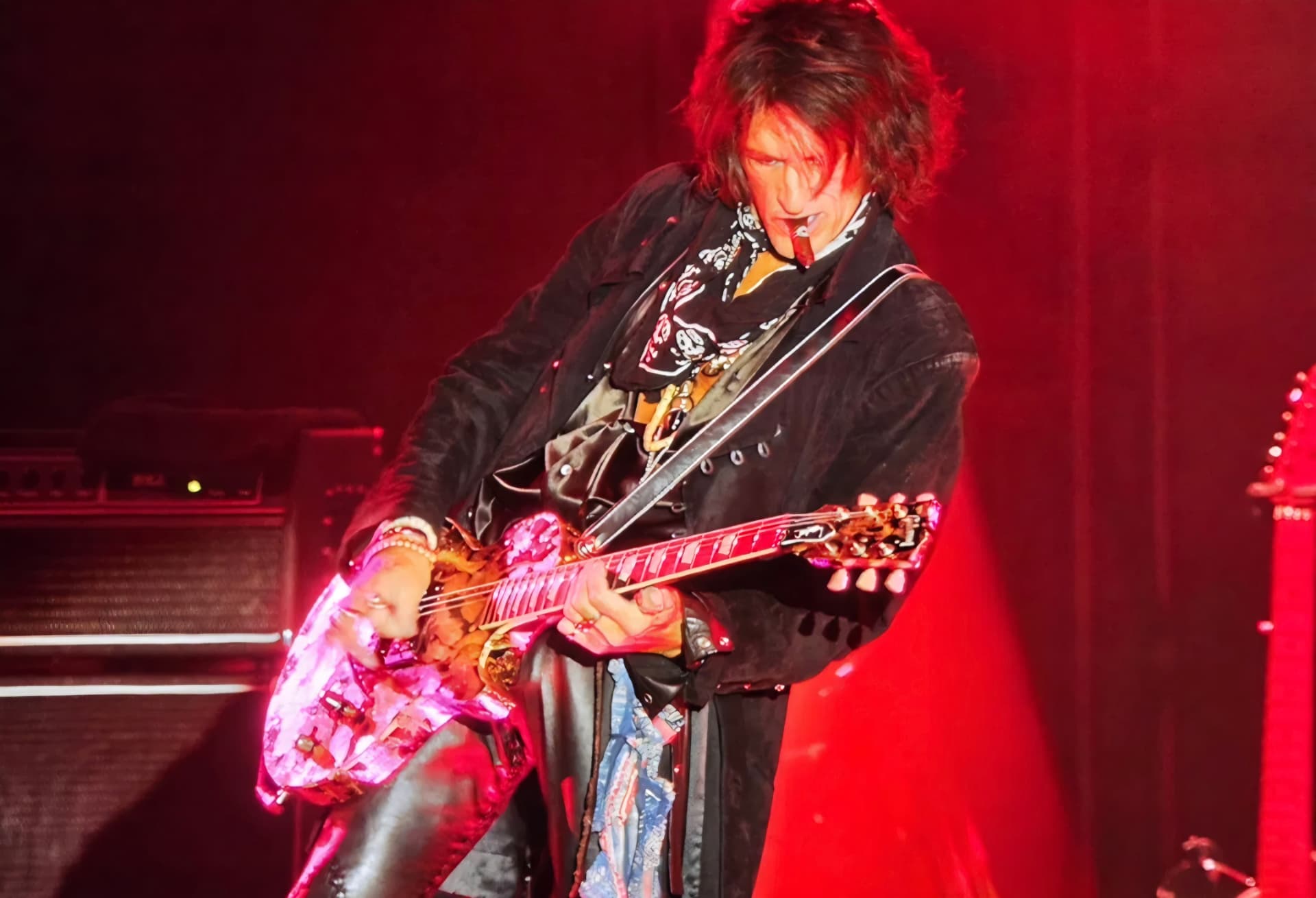 Joe Perry playing guitar under red stage lighting